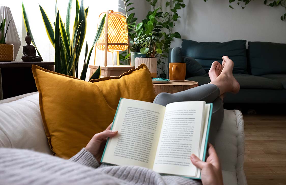 Young woman relaxing at home, lying on a sofa and reading a good book. 