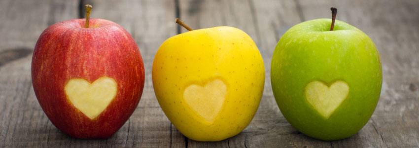 Three different coloured apples with hearts carved on them