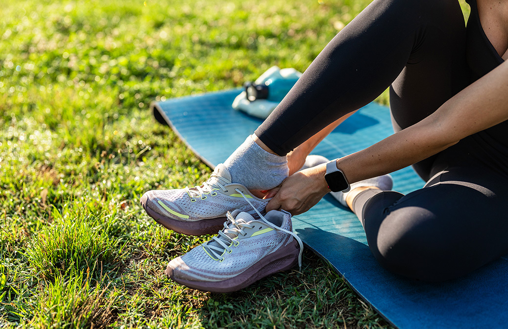 Young sporty woman sitting on a yoga mat in a park, tying her shoelaces after a workout.