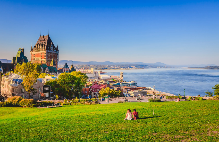 View of Old Quebec with historic buildings, green spaces and the St. Lawrence River under a clear blue sky on a summer evening.