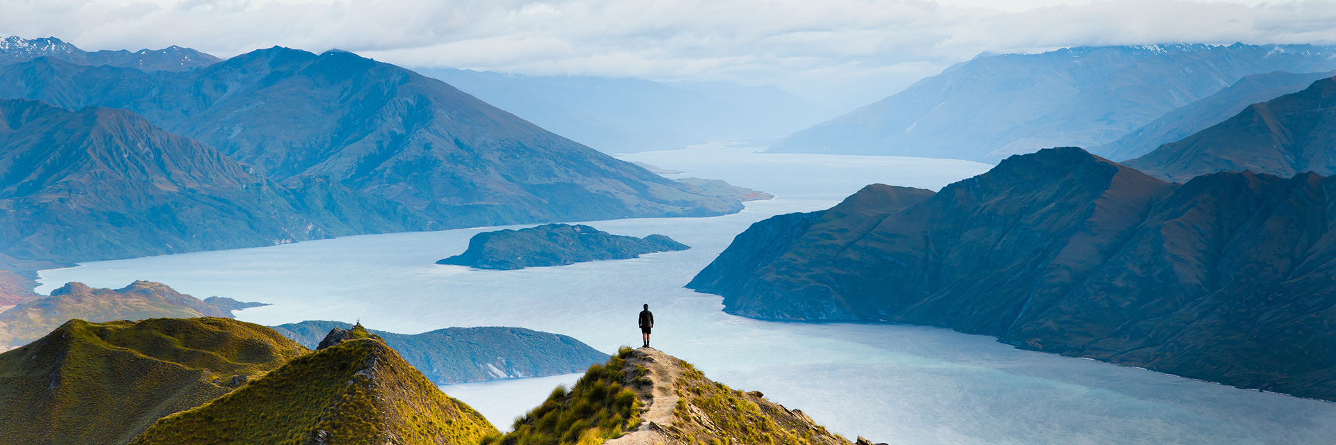 Person on top of a mountain looking at the view filled with mountains and a large body of water.